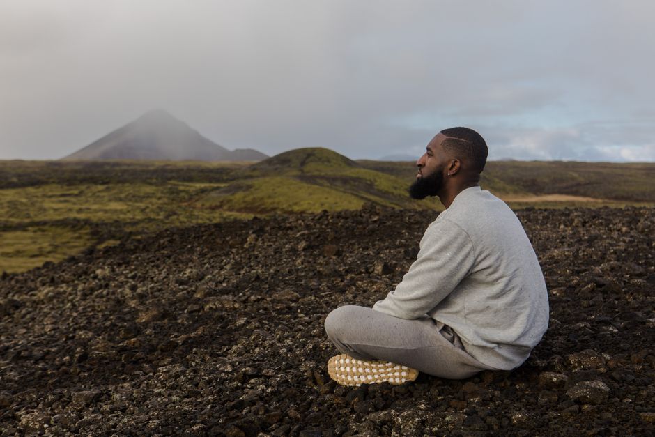 Man meditating on rocky terrain with mountain backdrop. Peace and tranquility outdoors.