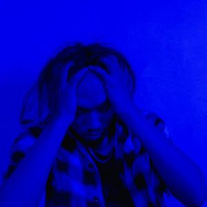 Portrait of a distressed person under dramatic blue lighting, expressing mental anguish.