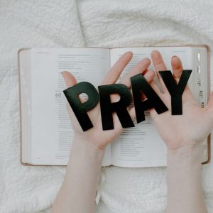 Hands holding 'PRAY' letters above an open Bible symbolizing faith and spirituality.