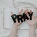 Hands holding 'PRAY' letters above an open Bible symbolizing faith and spirituality.