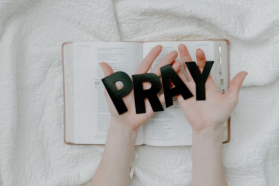 Hands holding 'PRAY' letters above an open Bible symbolizing faith and spirituality.