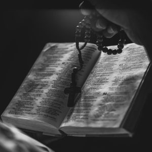 A black and white image of an open Bible with rosary beads, symbolizing faith and spirituality.