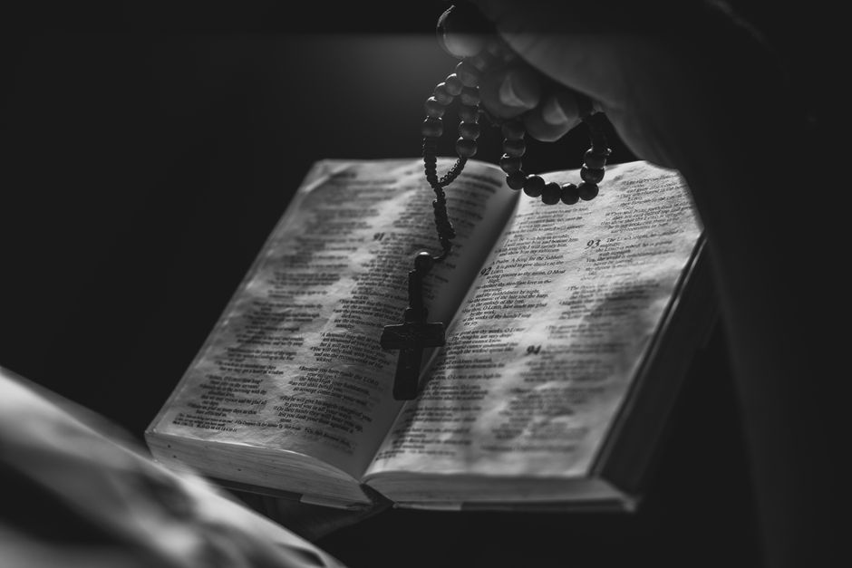 A black and white image of an open Bible with rosary beads, symbolizing faith and spirituality.