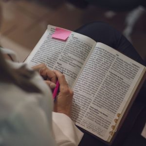 A woman reading a Bible with a pink note, captured indoors showing devotion and study.