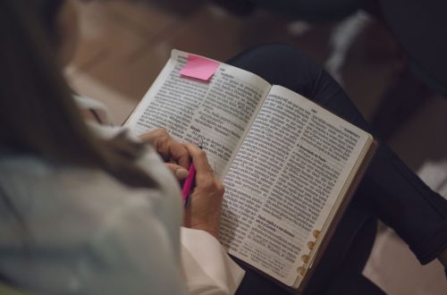 A woman reading a Bible with a pink note, captured indoors showing devotion and study.