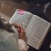 A woman reading a Bible with a pink note, captured indoors showing devotion and study.