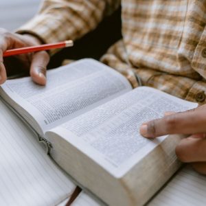 Hands holding an open Bible while taking notes with a pencil.