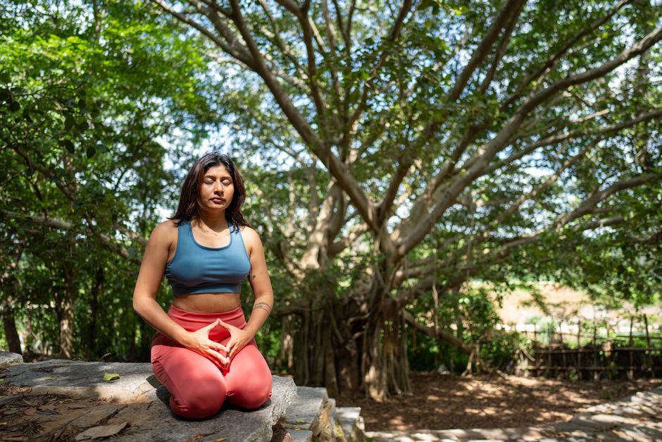 A woman practicing meditation under a banyan tree in nature, promoting tranquility and mindfulness.