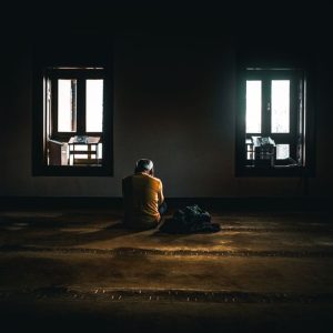 A solitary figure sits in contemplative silence in a dimly lit room with soft natural light.