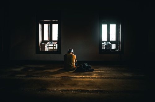 A solitary figure sits in contemplative silence in a dimly lit room with soft natural light.