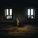 A solitary figure sits in contemplative silence in a dimly lit room with soft natural light.