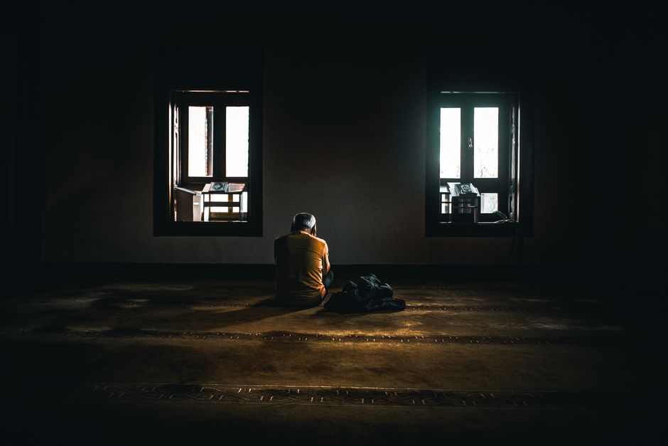 A solitary figure sits in contemplative silence in a dimly lit room with soft natural light.