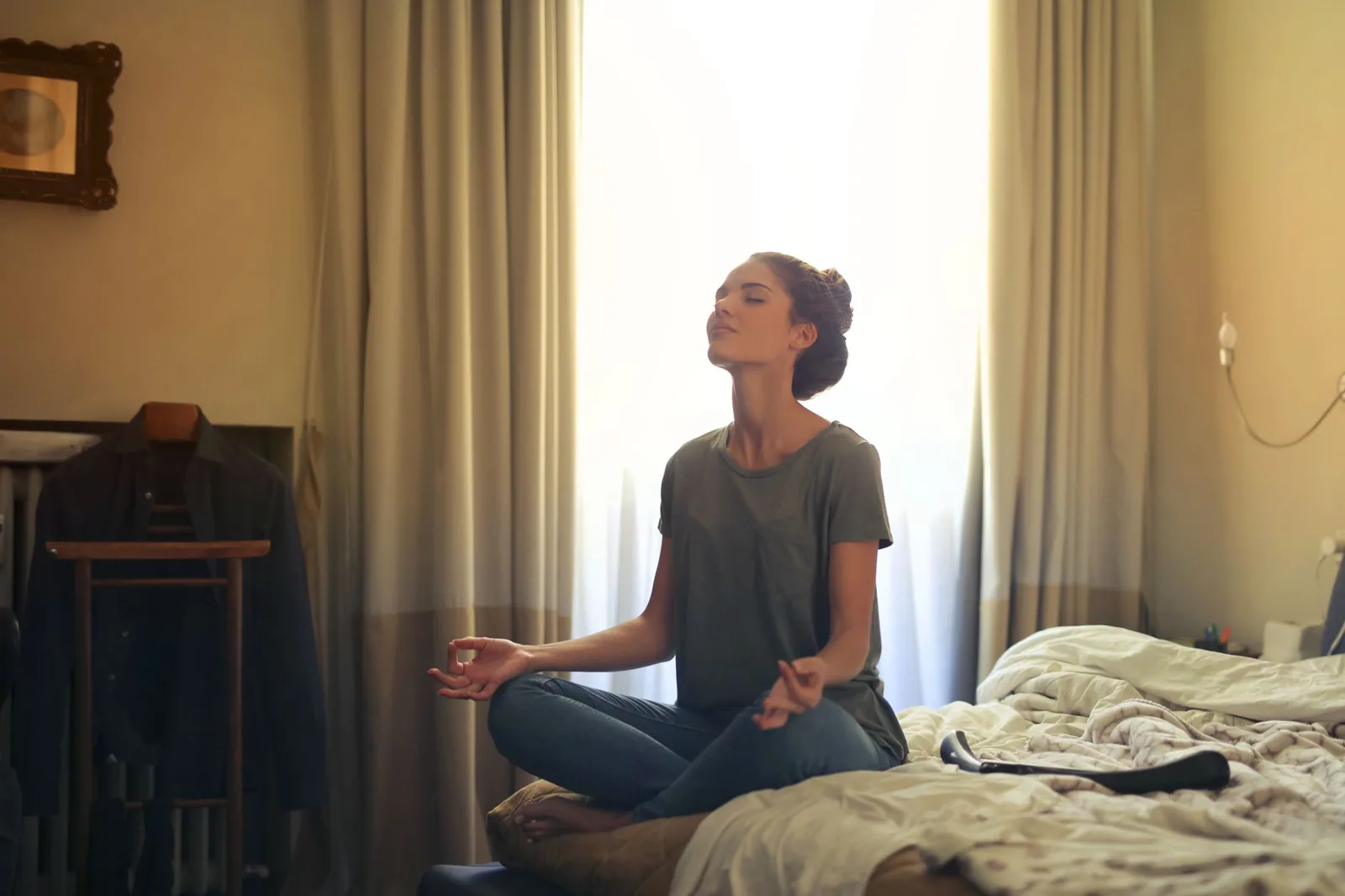 Mulher adulta meditando em sua cama, rodeada por um ambiente calmo e relaxante, perfeito para meditação